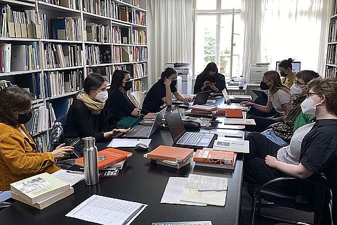 Neun Studierende sitzen an einem Tisch mit vielen Büchern und Laptops. Sie recherchieren oder diskutieren konzentriert. © HTW Berlin / Anna Warsinke