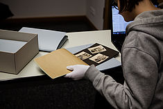 Studentin blättert mit der linken behandschuten Hand in einem alten Buch, mit der rechten Hand bedient sie eine Laptoptastatur
